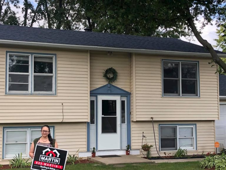 Homeowner with a Martin Exteriors yard sign in front of a two-story home