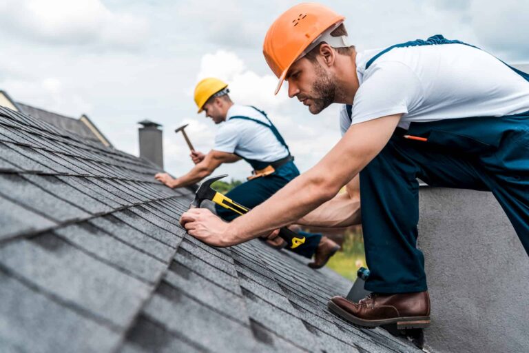 Two roofers in hard hats installing asphalt shingles