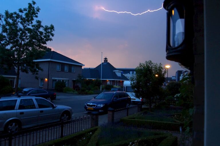 Lightning over a residential street with parked cars at dusk