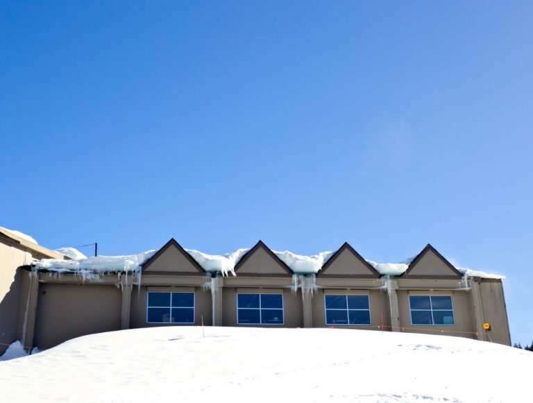Snow on a row of townhome roofs with icicles along the eaves