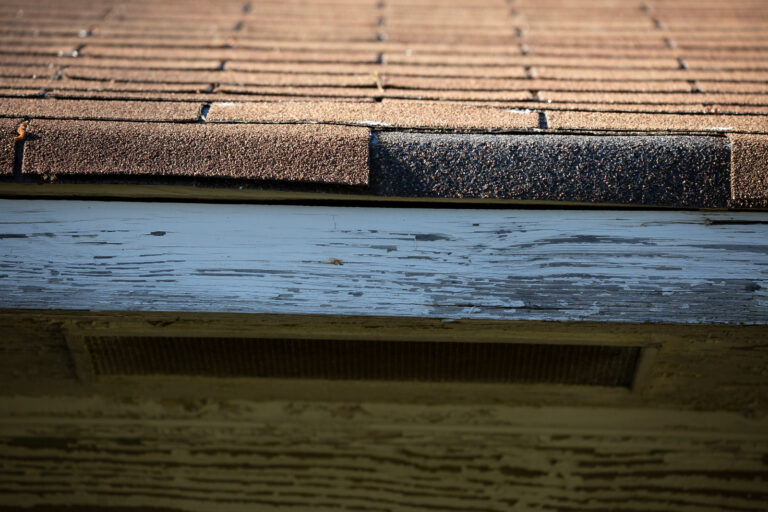 Close-up of a worn shingle edge above weathered fascia board