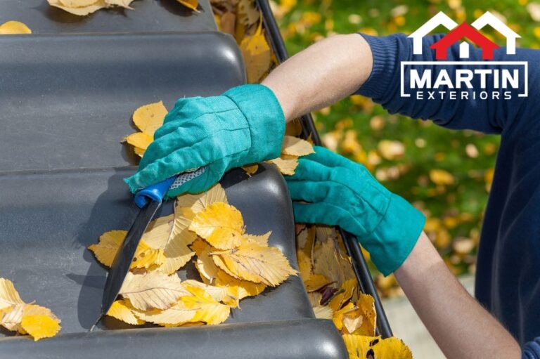 Gloved hands clearing wet fall leaves from the edge of a roof