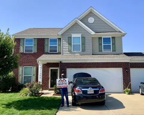 Homeowner with a Martin Exteriors sign in front of a two-story brick and siding home | Martin Exteriors