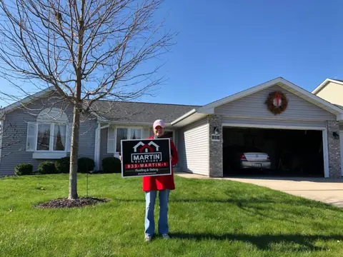 Homeowner holding a Martin Exteriors yard sign in front of a ranch home with a new roof | Martin Exteriors