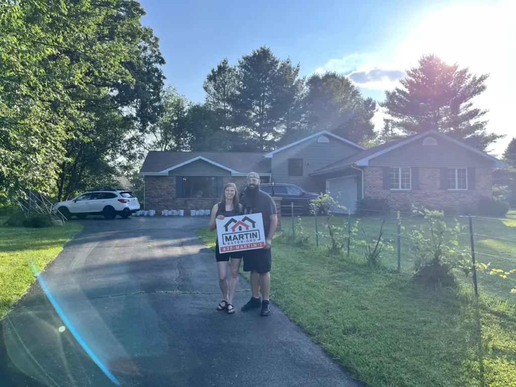 Homeowners holding a Martin Exteriors yard sign in front of their new roof and siding in Beloit, WI