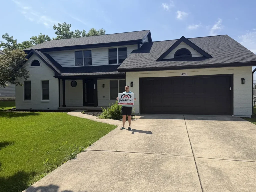 Happy Martin Exteriors Roofing & Siding customer holding a yard sign in front of their two-story home