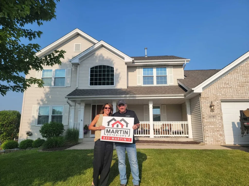 Happy Martin Exteriors Roofing & Siding customers holding a yard sign on the front porch of their two-story home