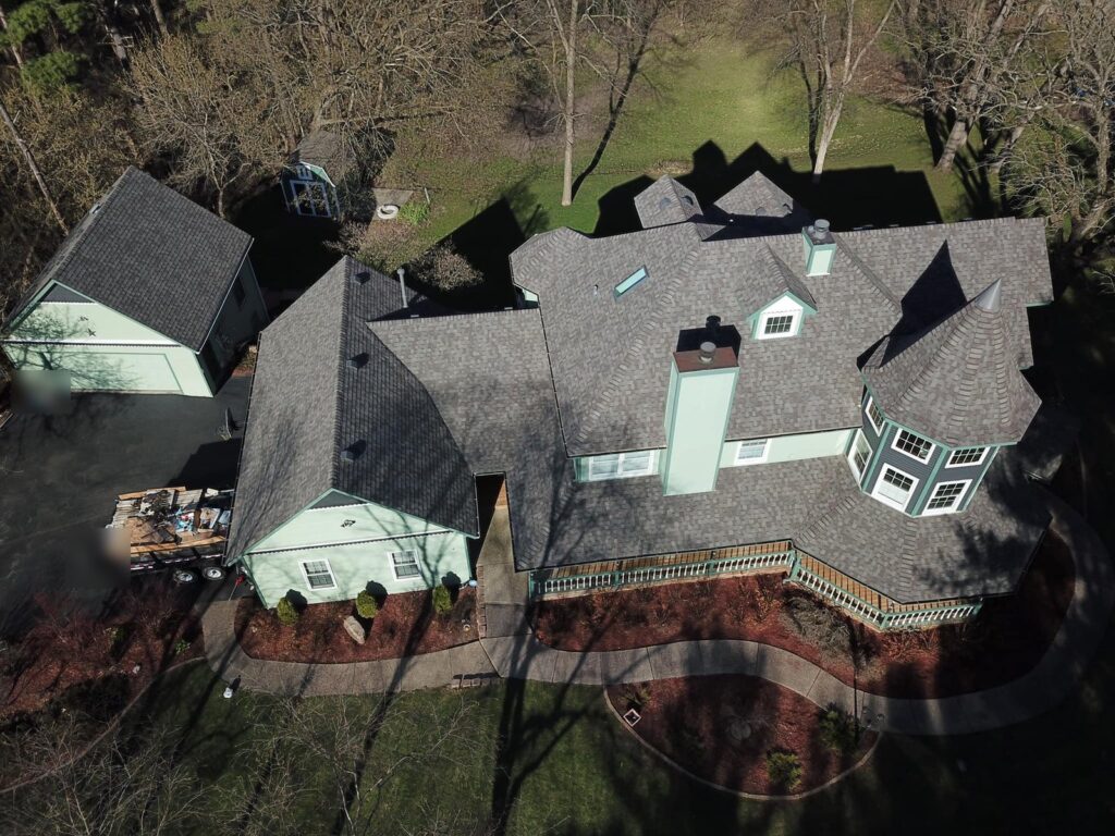 Aerial view of a new shingle roof by Martin Exteriors on a large home with a turret and a detached garage