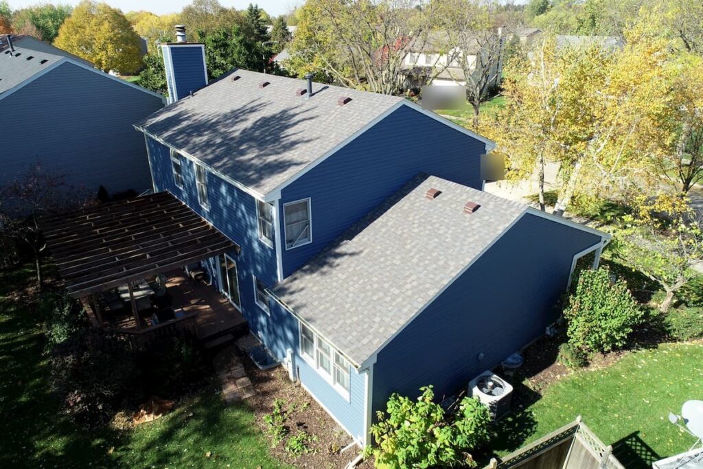 Aerial view of a finished shingle roof by Martin Exteriors on a blue two-story home