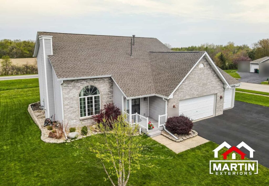 Aerial view of a shingle roof by Martin Exteriors on a home with gray brick and siding and an attached garage