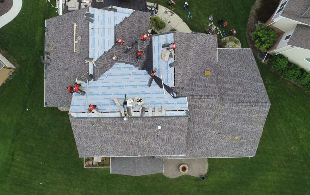 Aerial view of a Martin Exteriors crew laying new shingles over fresh underlayment on a large multi-gable roof