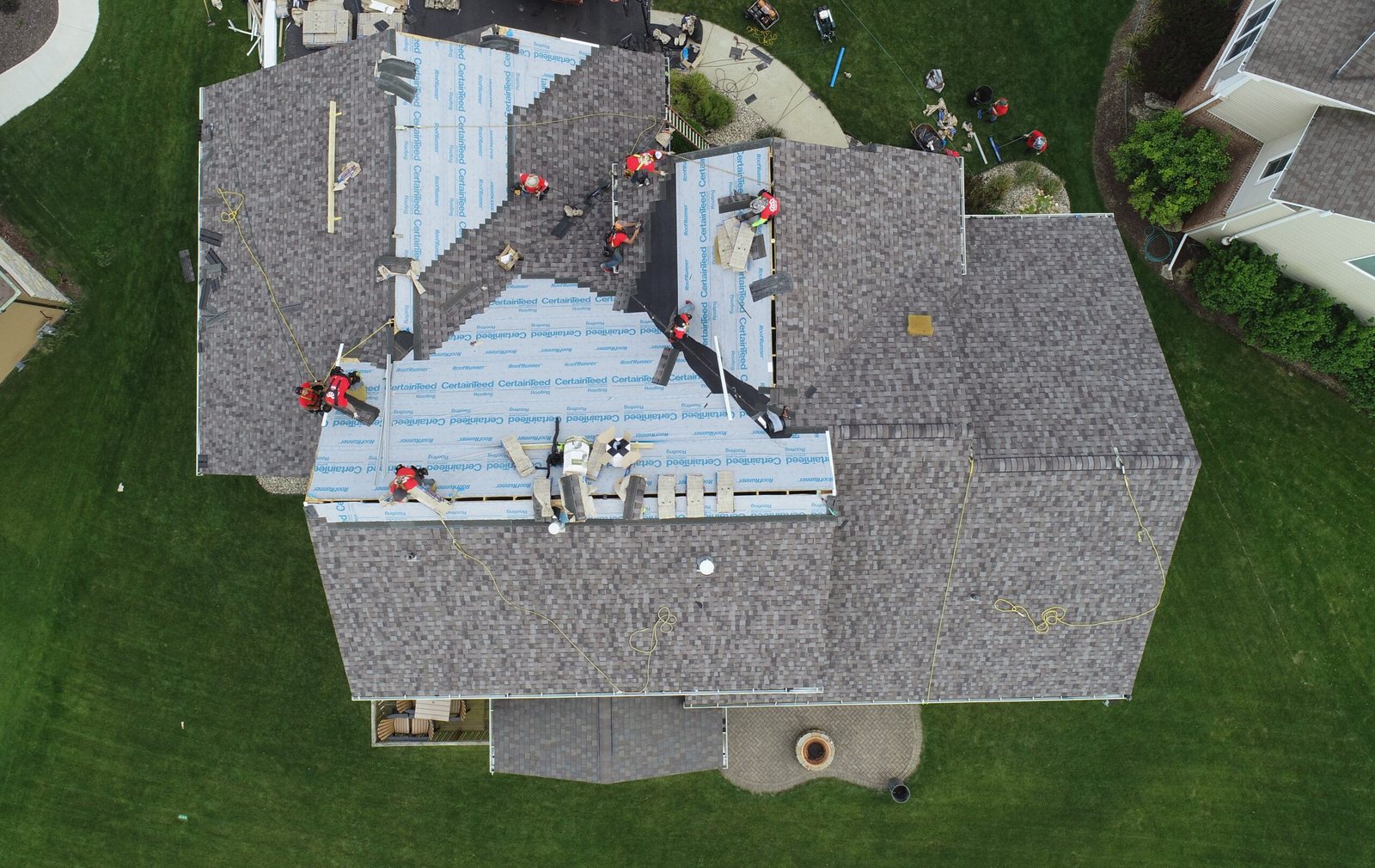 Aerial view of a Martin Exteriors crew laying new shingles over fresh underlayment on a large multi-gable roof
