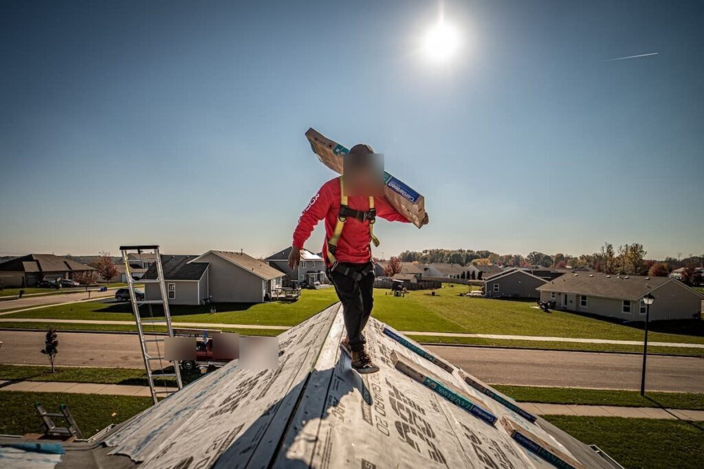 Martin Exteriors roofer carrying a bundle of shingles along a roof ridge covered in underlayment