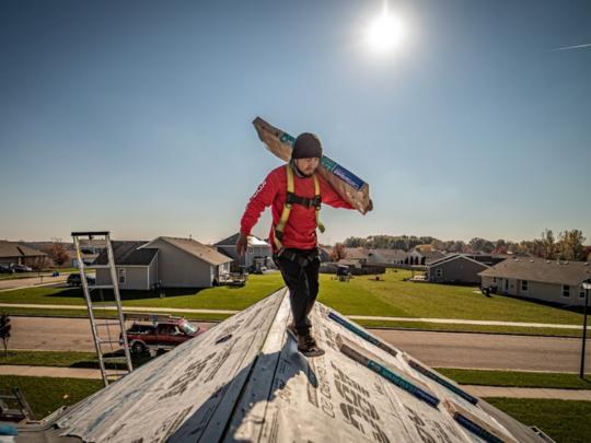 Martin Exteriors roofer in a safety harness carrying roofing material along the ridge of a house roof
