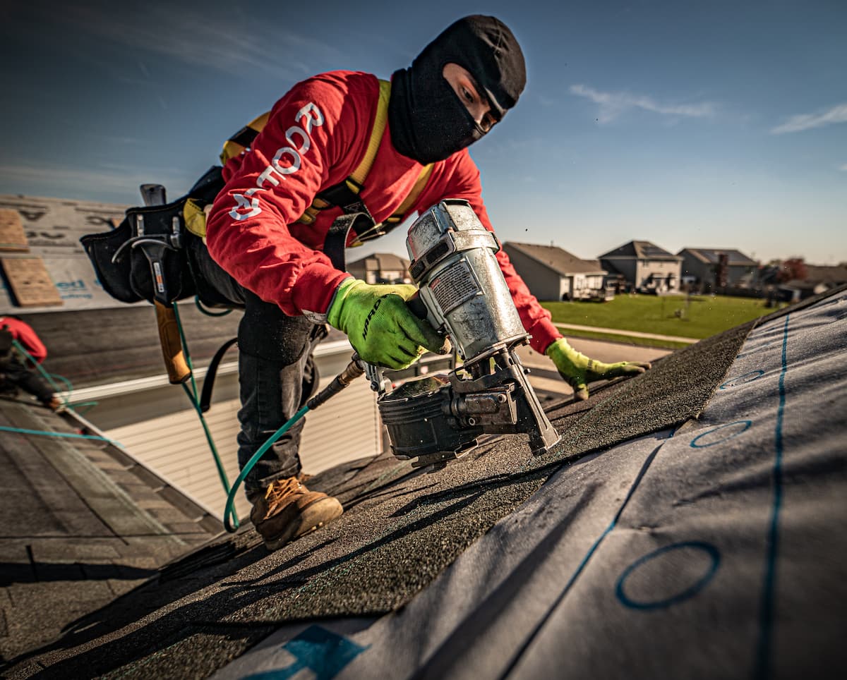 Martin Exteriors roofer in cold-weather gear nailing shingles on a roof in late fall