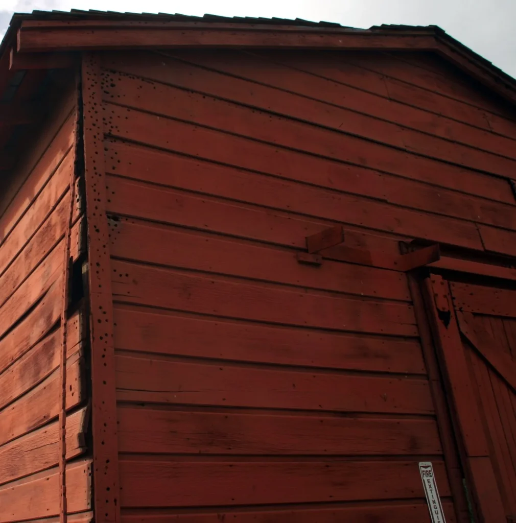 Corner trim board on red painted wood lap siding, peppered with small woodpecker holes